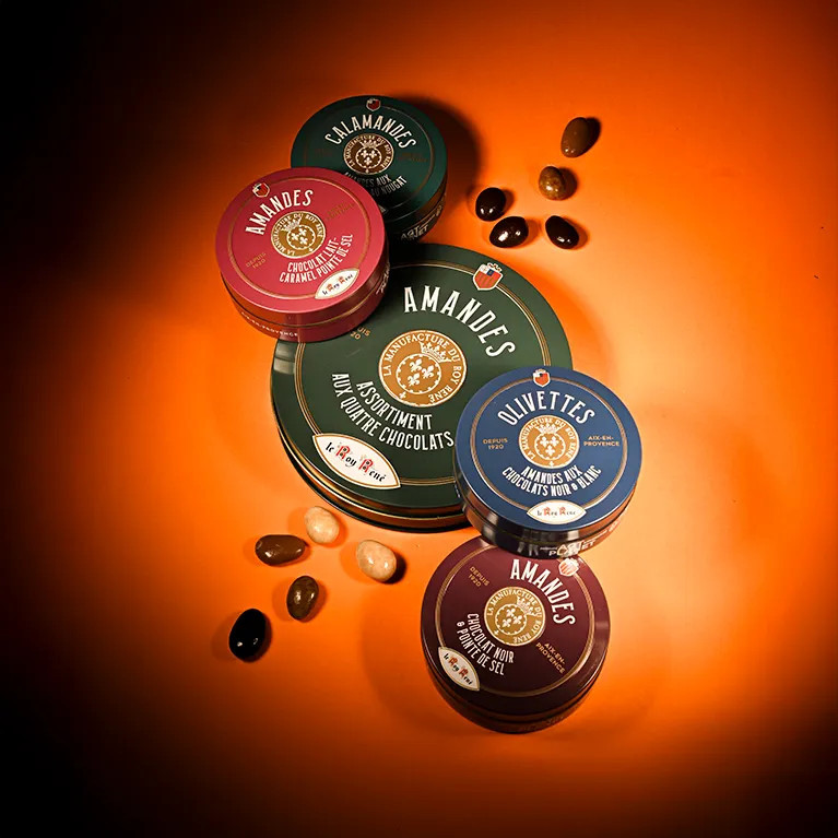 Coffret assortiment d’enrobés au chocolat avec quelques amandes enrobées disposées autour.